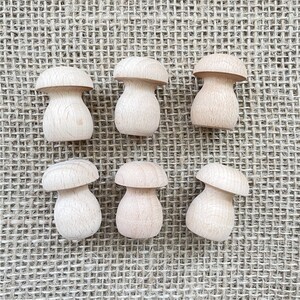 K&ouml;nnte beinhalten: Sechs h&ouml;lzerne Pilzformen, in nat&uuml;rlicher Holzfarbe lackiert, sind auf einem Jute-Hintergrund angeordnet.