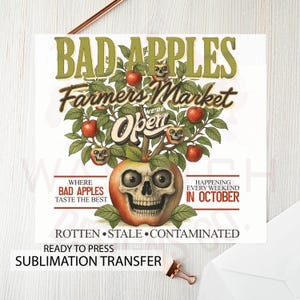 May include: A sublimation transfer design featuring a stylized apple with a skull face, surrounded by red apples and green leaves. The text reads "BAD APPLES Farmers Market" and "Happening Every Weekend in October."