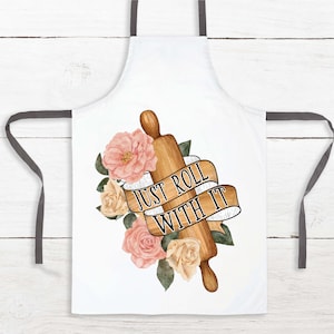 May include: White kitchen apron with a gray adjustable strap. The apron features a watercolor illustration of a rolling pin with pink and cream flowers and a banner that reads "Just Roll With It".