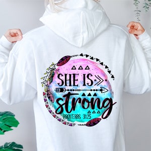 May include: White hooded sweatshirt with a colourful graphic design featuring an arrow, feathers, and the text "SHE IS> strong PROVERBS 31:25".