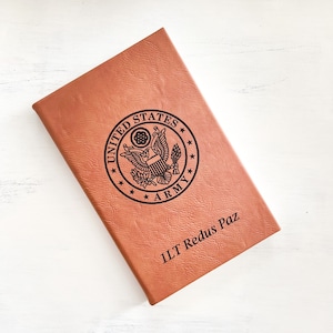 May include: A brown leather journal with the United States Army seal and the text "1LT Redus Paz" engraved on the front.