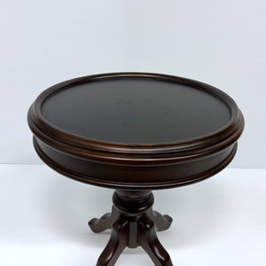 May include: A dark brown, round side table with a three-legged base. The tabletop is approximately 24 inches in diameter. The table has a classic design, suitable for various interior styles.