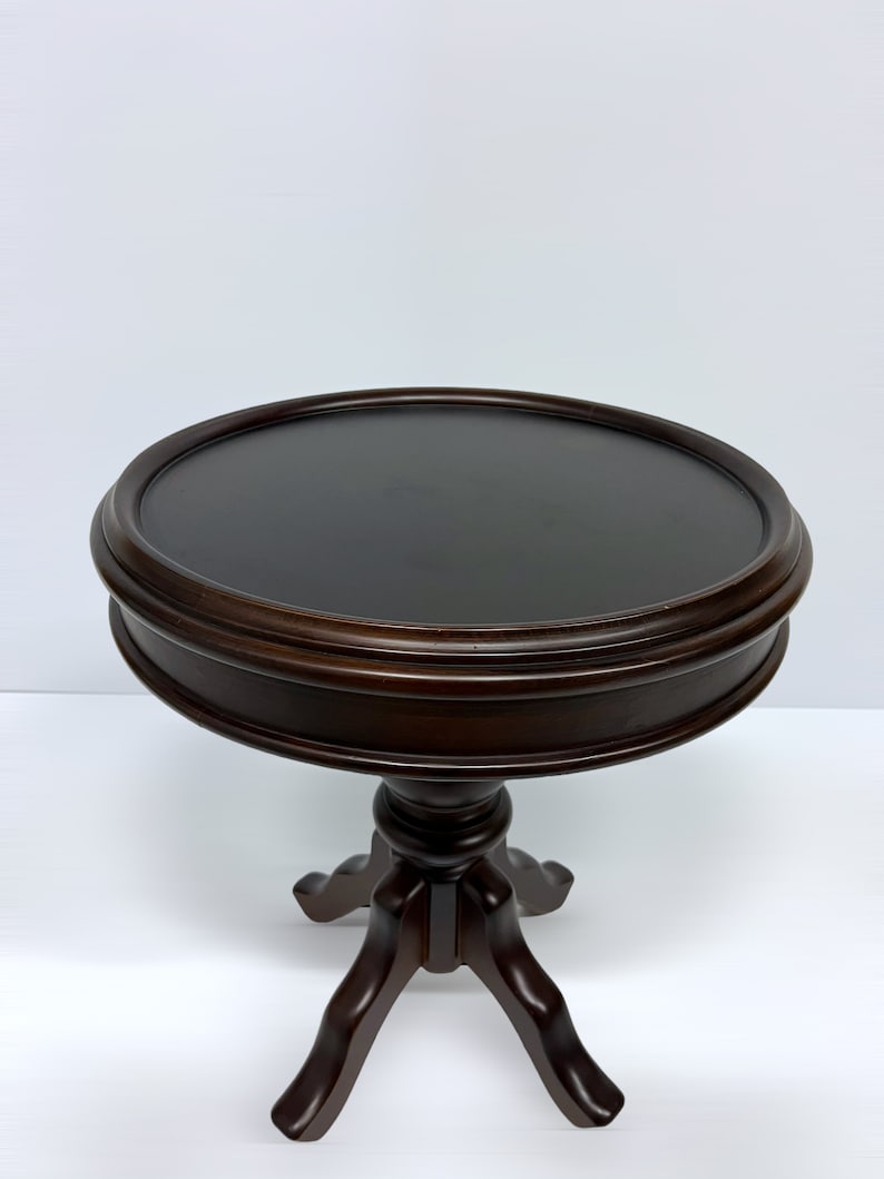 May include: A dark brown, round side table with a three-legged base. The tabletop is approximately 24 inches in diameter. The table has a classic design, suitable for various interior styles.