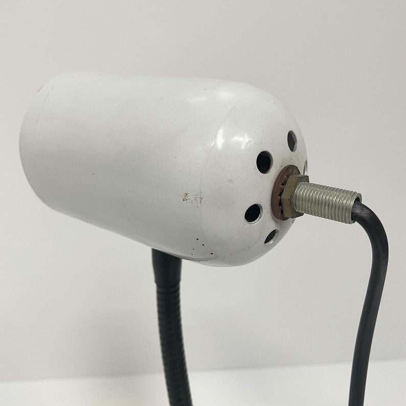 May include: White desk lamp with a flexible black arm and a white cylindrical shade with multiple holes. The lamp has a black cord.