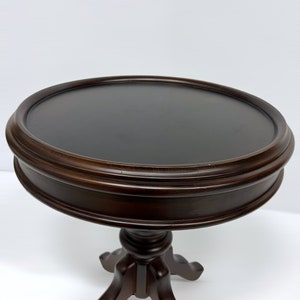 May include: A dark brown, round side table with a pedestal base. The tabletop is approximately 24 inches in diameter. The table has a classic design, suitable for various interior styles.