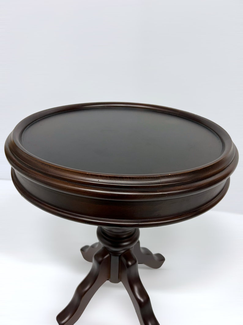 May include: A dark brown, round side table with a pedestal base. The tabletop is approximately 24 inches in diameter. The table has a classic design, suitable for various interior styles.