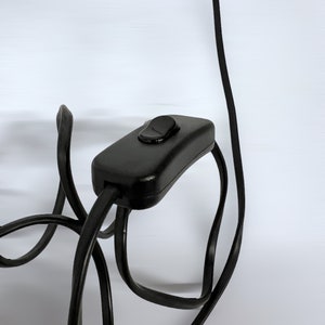 Może przedstawiać: Czarny przew&oacute;d elektryczny z wbudowanym włącznikiem/wyłącznikiem.