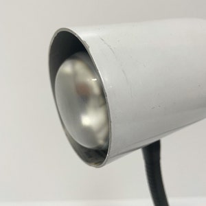 May include: A white metal desk lamp with a black cord. The lamp has a round, white shade with a clear glass bulb.
