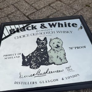 Pode incluir: Espelho preto e branco com moldura preta. Apresenta um gráfico de dois cães e o texto "Black & White Choice Old Scotch Whisky". O texto também inclui "Product of Scotland" e "70° Proof".