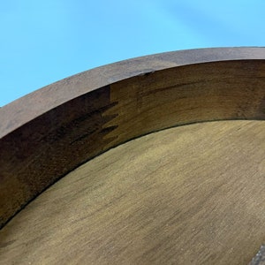 May include: Close-up of a wooden object with a curved, dark brown edge and a lighter brown interior. The edge features a dovetail joint, showcasing the craftsmanship. The background is a clear blue sky.