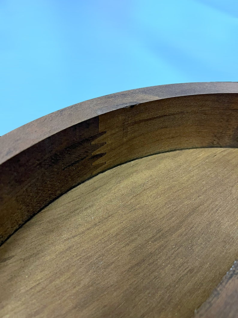 May include: Close-up of a wooden object with a curved, dark brown edge and a lighter brown interior. The edge features a dovetail joint, showcasing the craftsmanship. The background is a clear blue sky.