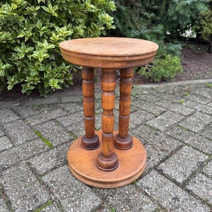 Peut inclure: Une petite table ronde en bois avec trois pieds tournés. La table est en bois brun clair et a un design simple et classique.