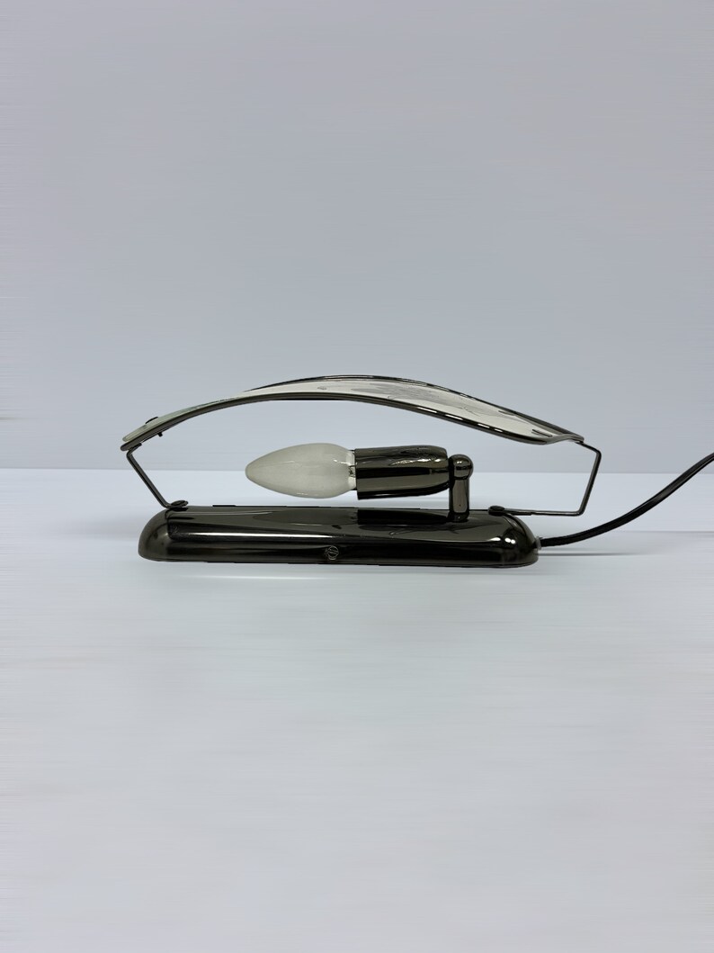 Może przedstawiać: Czarna metalowa lampa biurkowa z zakrzywionym ramieniem i białą żar&oacute;wką. Lampa ma czarny przew&oacute;d i czarną podstawę.