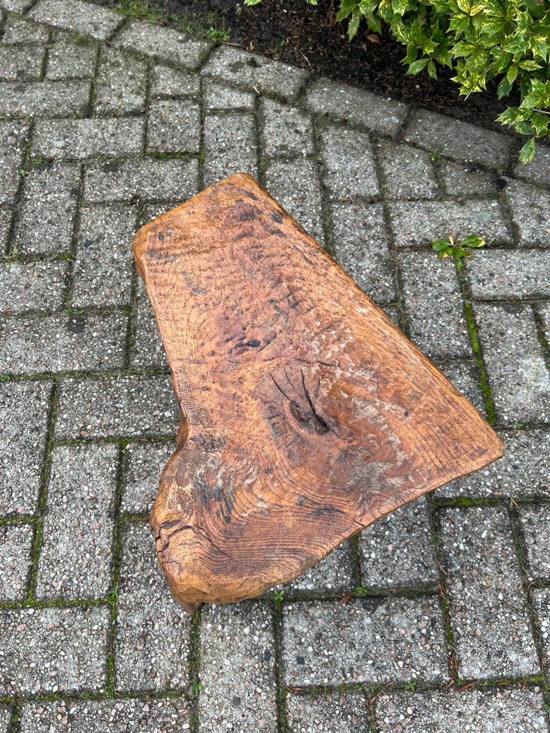 Puede incluir: Un taburete de madera r&uacute;stico con una forma natural irregular y un acabado marr&oacute;n oscuro. El taburete est&aacute; hecho de una sola pieza de madera y tiene un aspecto &uacute;nico hecho a mano.