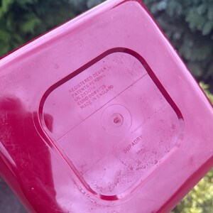 May include: A close-up of the bottom of a red plastic container. The text "REGISTERED DESIGN PATENTS PENDING UK 2113074 EURO 0089733 MADE IN ENGLAND" is printed on the bottom. The word "SUPADRY" is also visible.