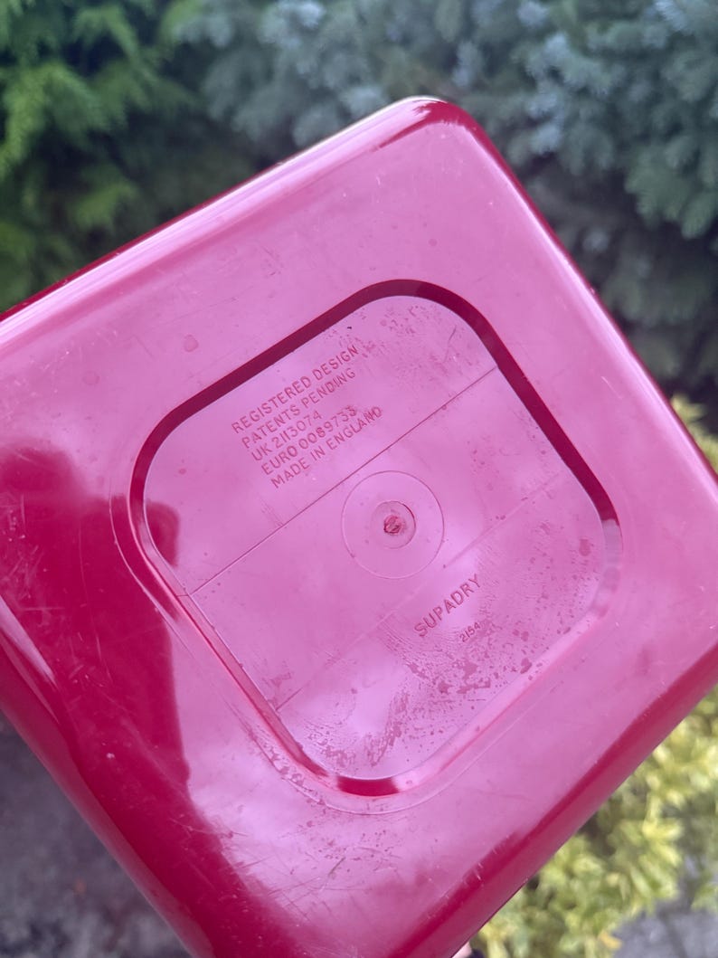 May include: A close-up of the bottom of a red plastic container. The text "REGISTERED DESIGN PATENTS PENDING UK 2113074 EURO 0089733 MADE IN ENGLAND" is printed on the bottom. The word "SUPADRY" is also visible.