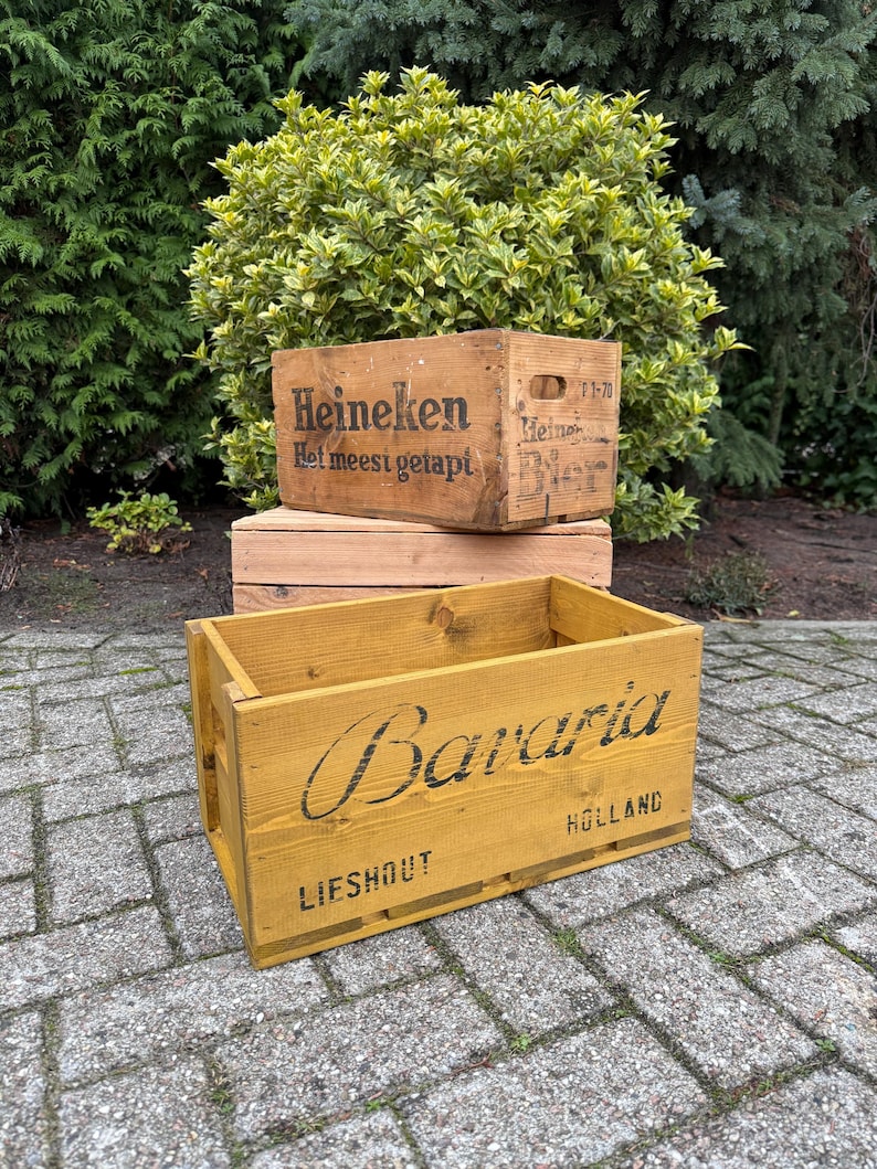 May include: Two wooden crates, one with the word "Heineken" and the phrase "Het meest getapt" printed on it. The other crate is painted yellow with the word "Bavaria" and the word "Holland" printed on it.