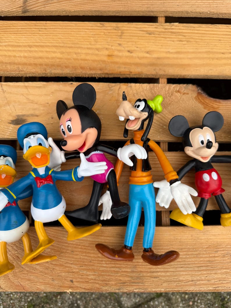 Pode incluir: Uma cole&ccedil;&atilde;o de figuras de personagens da Disney, incluindo Mickey Mouse, Minnie Mouse, Pato Donald e Pateta. As figuras s&atilde;o coloridas e posam em v&aacute;rias poses. As figuras s&atilde;o feitas de pl&aacute;stico e s&atilde;o exibidas em uma superf&iacute;cie de madeira.
