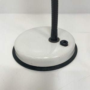 May include: A white desk lamp with a black flexible arm and a black base. The lamp has a white enamel finish and a black power cord.