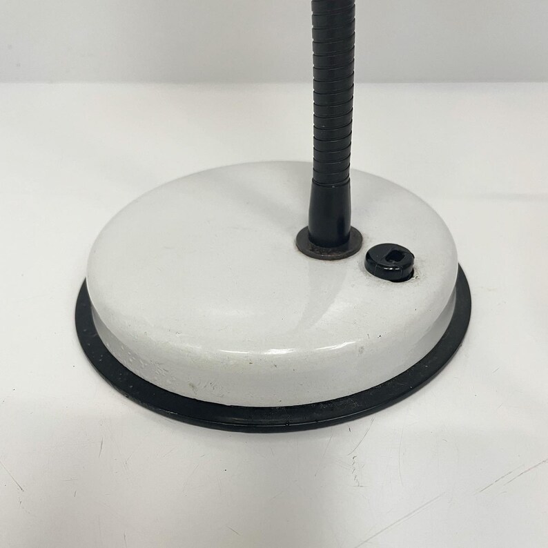 May include: A white desk lamp with a black flexible arm and a black base. The lamp has a white enamel finish and a black power cord.