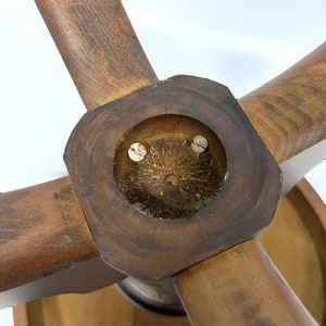 May include: Close-up of a wooden object with four spokes radiating from a central hub. The wood has a warm, brown tone with visible grain. The hub features a circular inset with two screws. The object appears to be part of a larger piece.