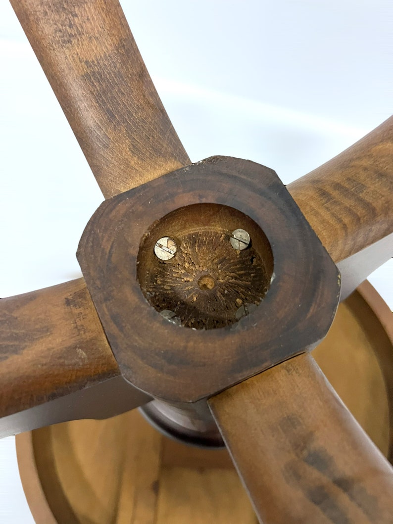May include: Close-up of a wooden object with four spokes radiating from a central hub. The wood has a warm, brown tone with visible grain. The hub features a circular inset with two screws. The object appears to be part of a larger piece.