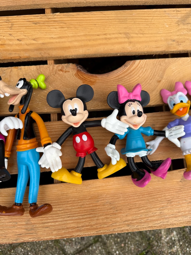 Pode incluir: Uma cole&ccedil;&atilde;o de figuras de personagens da Disney, incluindo Mickey Mouse, Minnie Mouse, Pateta e Margarida. Mickey usa cal&ccedil;as vermelhas e sapatos amarelos. Minnie usa um vestido azul e um la&ccedil;o rosa. Pateta tem um colete laranja e cal&ccedil;as azuis. Margarida usa um top roxo e um la&ccedil;o rosa.