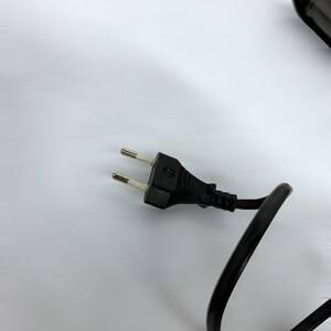 Może przedstawiać: Czarny przew&oacute;d elektryczny z wtyczką europejską z dwoma bolcami.