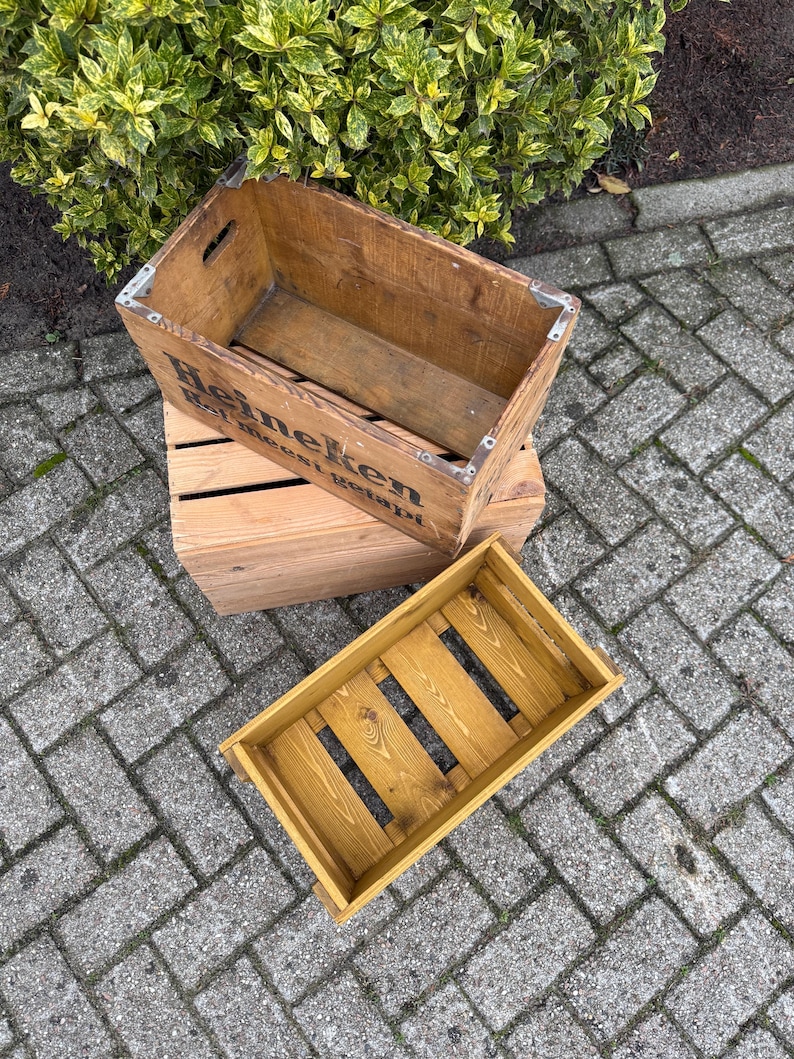 May include: Three wooden crates of different sizes. The largest crate has the word "Heineken" printed on the side. The crates are made of wood and have a rustic appearance. The smallest crate is painted yellow.