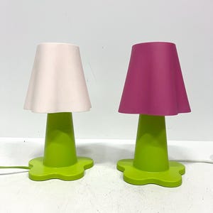 May include: Two table lamps with green bases and flower-shaped bases. One lamp has a pink lampshade and the other has a white lampshade.