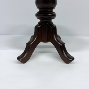 May include: A dark brown wooden pedestal table with a turned column and three curved legs. The table has a classic design and is suitable for various decorative purposes. The table's height is approximately 30 inches.