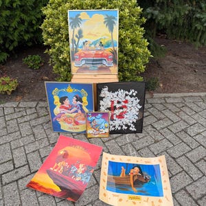 Op de afbeelding: Een verzameling ingelijste Disney-kunstprints met verschillende personages en scènes. Inclusief een print van Mickey en Minnie Mouse in een rode cabriolet, Sneeuwwitje, Aladdin, De Leeuwenkoning, Pocahontas en een print met Dalmatische thema's.