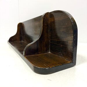 Könnte beinhalten: Ein dunkelbraunes Holzregal mit zwei Regalbrettern. Das Regal ist auf der rechten Seite gebogen und hat ein schlichtes Design.