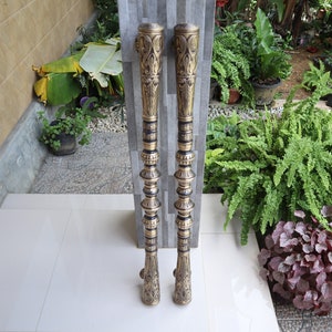 May include: A pair of ornate gold door handles with intricate black designs. The handles are tall and slender, with a decorative knob at the top.