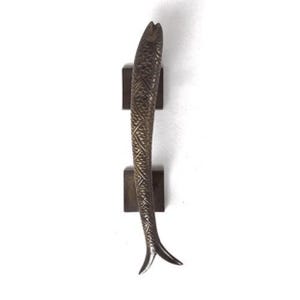 May include: A bronze fish-shaped door handle with a detailed pattern on its surface. The handle is mounted on two square wooden blocks.