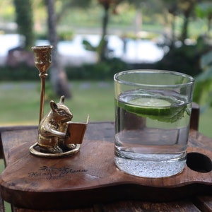 Könnte beinhalten: Ein Holztablett mit einer kleinen Messingmausfigur, die ein Buch liest, einem Glas Wasser mit einer Gurkenscheibe und dem Text "Relax & Enjoy" auf dem Tablett.
