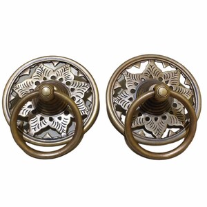 Puede incluir: Dos tiradores de puerta de latón antiguo con diseños florales ornamentados y un asa de anillo. Los tiradores tienen una base circular con un centro elevado y un asa de anillo.