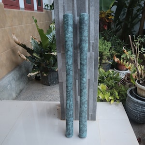 May include: Two long, decorative, teal-coloured metal cylinders with intricate designs. The cylinders are standing upright on a tiled floor.
