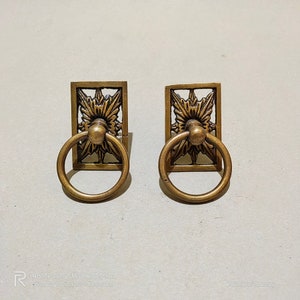 May include: Two gold-toned metal drawer pulls with ornate floral designs and ring handles.