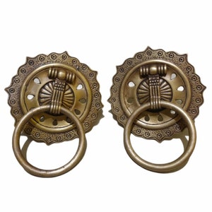 May include: A pair of ornate brass door handles with a ring pull. The handles have a decorative design with a central motif and a scalloped edge.