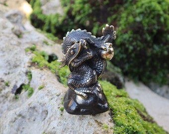 May include: A small, black bronze dragon figurine holding a golden orb. The dragon is sitting on a rock with moss growing on it.