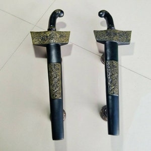Peut inclure: Deux poignées de porte noires avec des accents dorés. Les poignées sont en forme d'épées avec des motifs complexes.