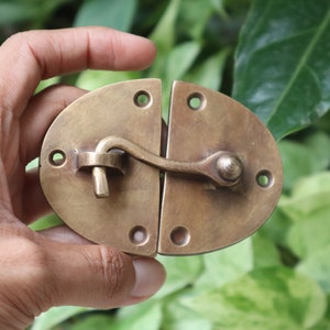 May include: A brass latch with a curved handle and two oval plates. The latch is closed and the handle is in the down position.