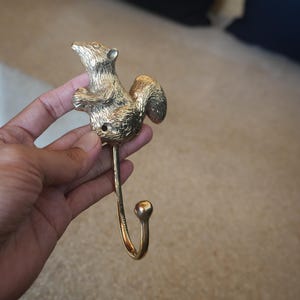 May include: A gold-colored squirrel hook with a detailed design. The hook is made of metal and has a curved shape.