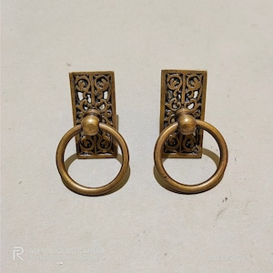May include: Two antique brass cabinet door pulls with ornate floral designs and a ring handle.