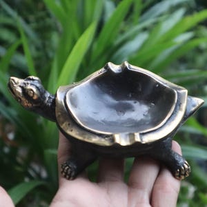 May include: A bronze turtle ashtray with a gold rim. The turtle is walking with its head up and its legs outstretched.