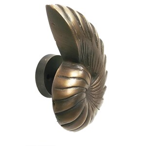May include: A bronze nautilus shell door knocker with a detailed, textured surface. The knocker is mounted on a round, black base.