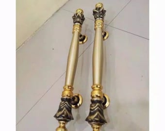 May include: A pair of gold door handles with ornate black accents. The handles are long and slender with a rounded top and a decorative base.