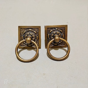 May include: Two antique brass cabinet door pulls with ornate square plates and ring handles.