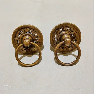 May include: Two antique brass door knobs with ornate floral designs and ring pulls.